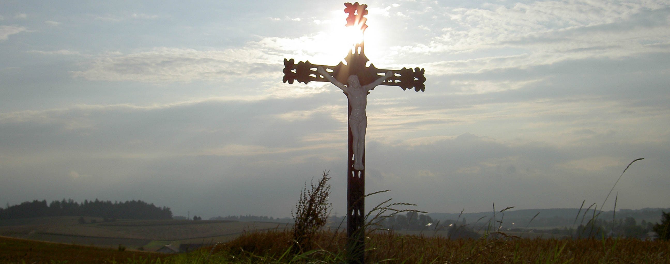 Ein Feldkreuz mit Sonne im Hintergrund